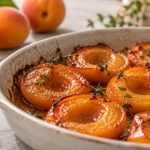 Demi-abricots rôtis dans un plat clair, avec des abricots frais en arrière-plan.